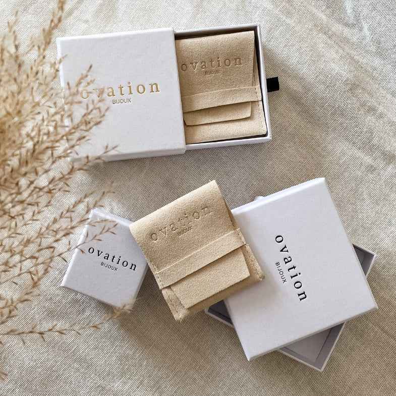 Écrin et pochette beige Ovation Bijoux présentés dans des boîtes blanches élégantes – packaging raffiné pour bijoux en plaqué or